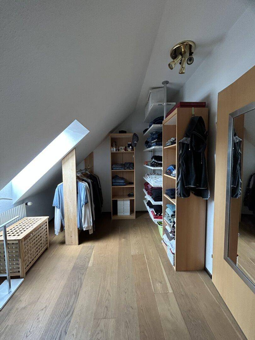 Geräumiger begehbarer Kleiderschrank im Dachgeschoss mit Regalen und Holzboden.