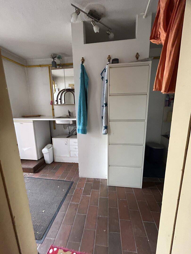 Hauswirtschaftsraum mit Waschbecken, kleinem Kühlschrank und Fliesenboden.