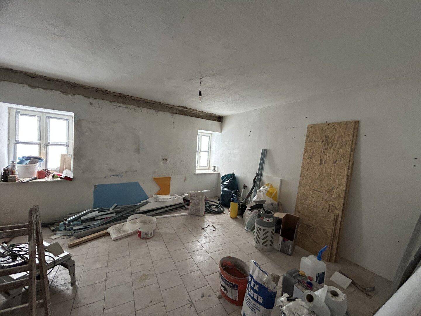 Raum im Rohbauzustand mit Fliesenboden und Fenstern, bereit zur Renovierung.