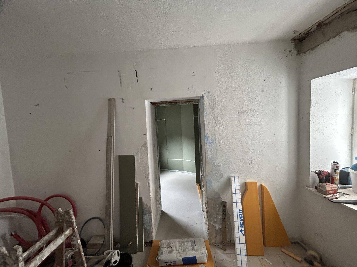 Raum im Rohbauzustand mit Türöffnung und Baumaterialien, bereit zur Renovierung.