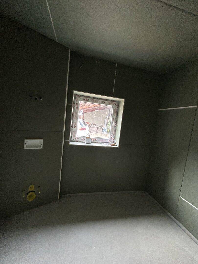 Badezimmer im Rohbau mit Fenster und vorbereiteten Installationen.