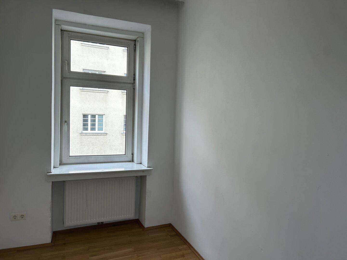 Heller Raum mit weiß gestrichenen Wänden, Holzfußboden und einem Fenster mit Heizkörper.