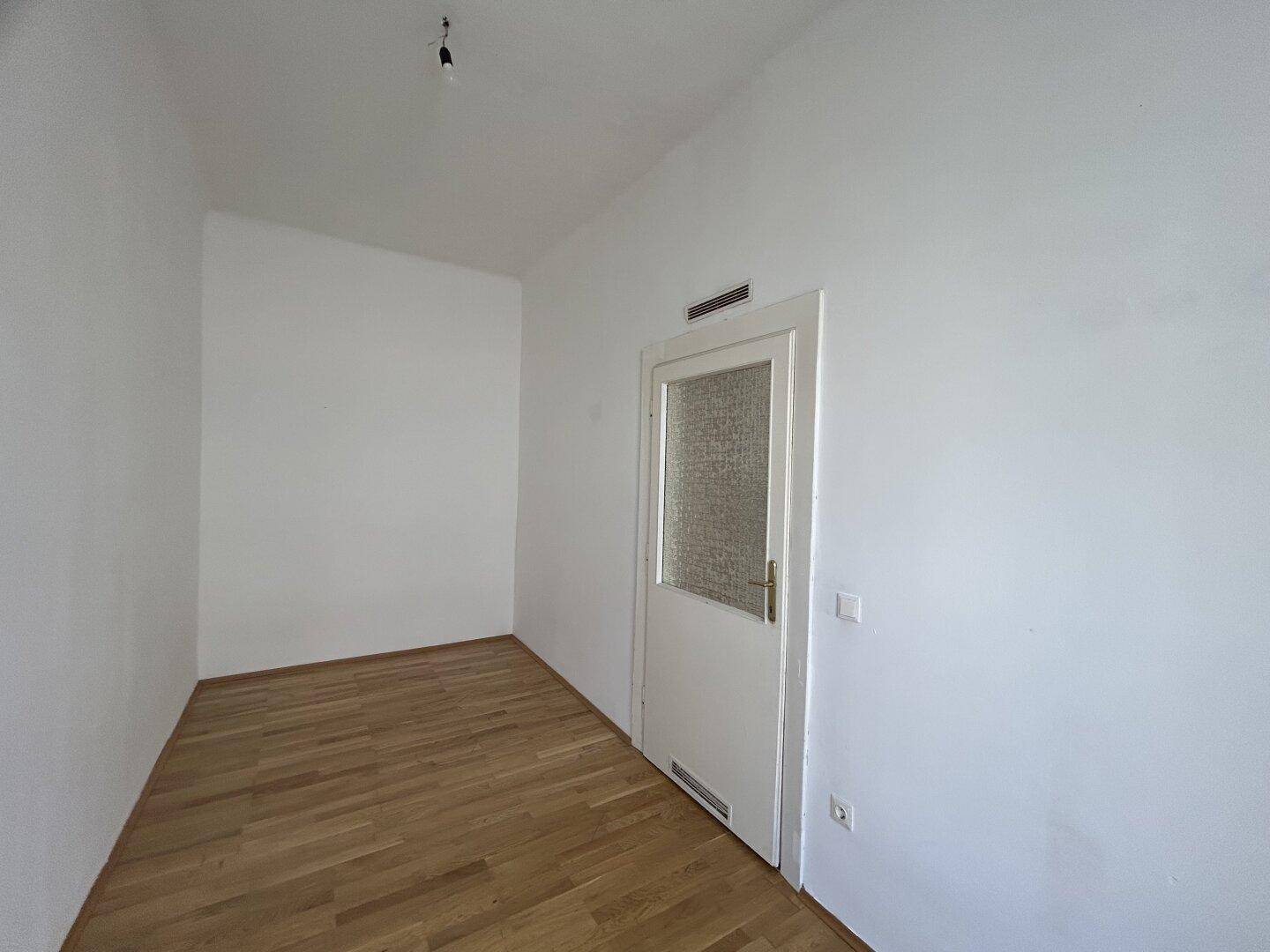 Leerer Raum mit weiß gestrichenen Wänden, Holzfußboden und einer Tür mit Glaseinsatz.
