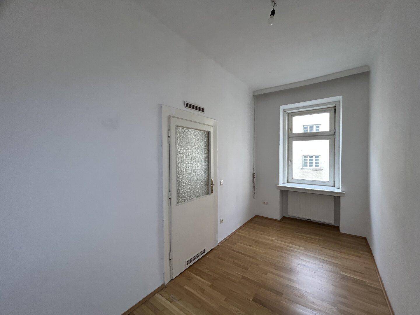 Heller Raum mit weiß gestrichenen Wänden, Holzfußboden, einer Tür und einem Fenster.