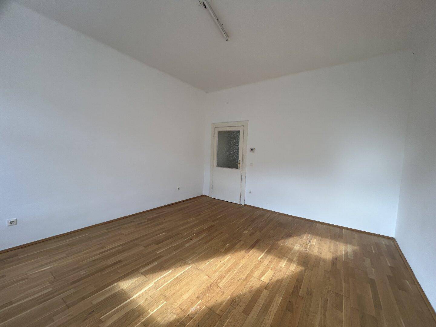 Leerer Raum mit Holzfußboden, einer Tür mit Glaseinsatz und natürlichem Lichteinfall.