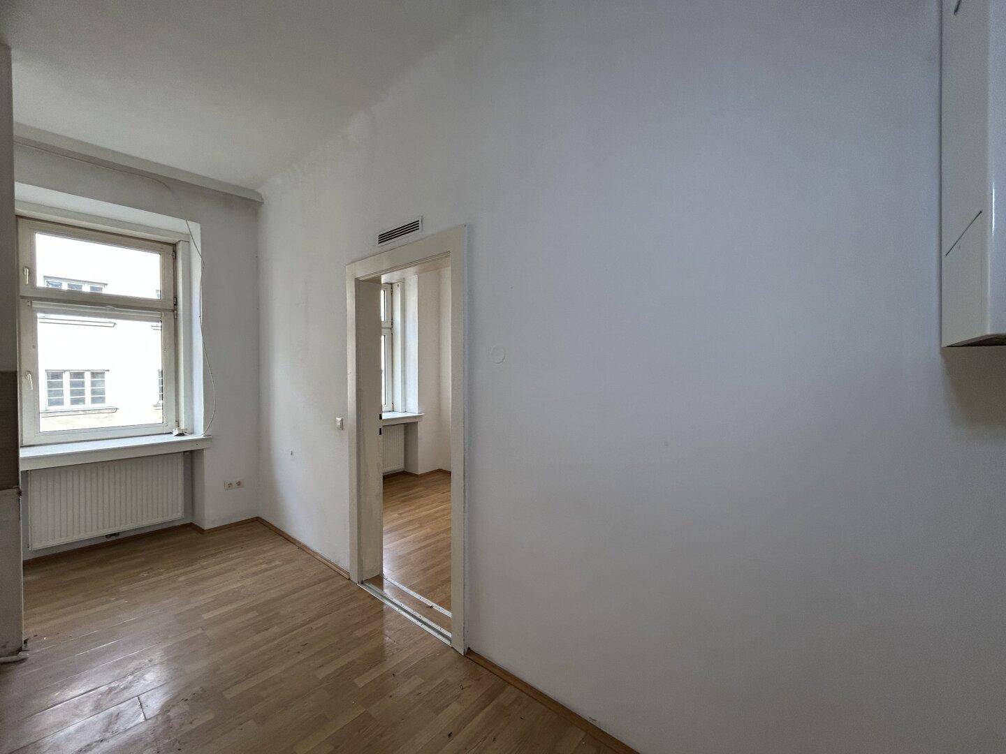 Heller Raum mit Holzfußboden und einem offenen Durchgang zu einem weiteren Zimmer.
