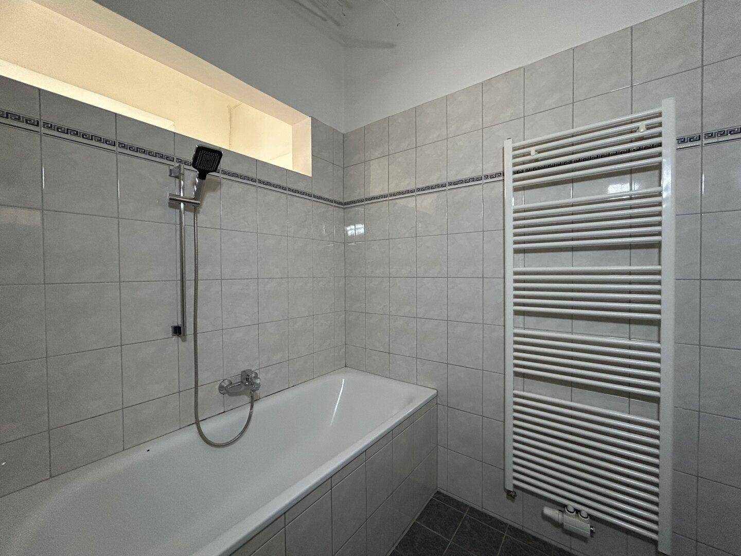Badezimmer mit Badewanne, Duschkopf und einem praktischen beheizten Handtuchhalter.