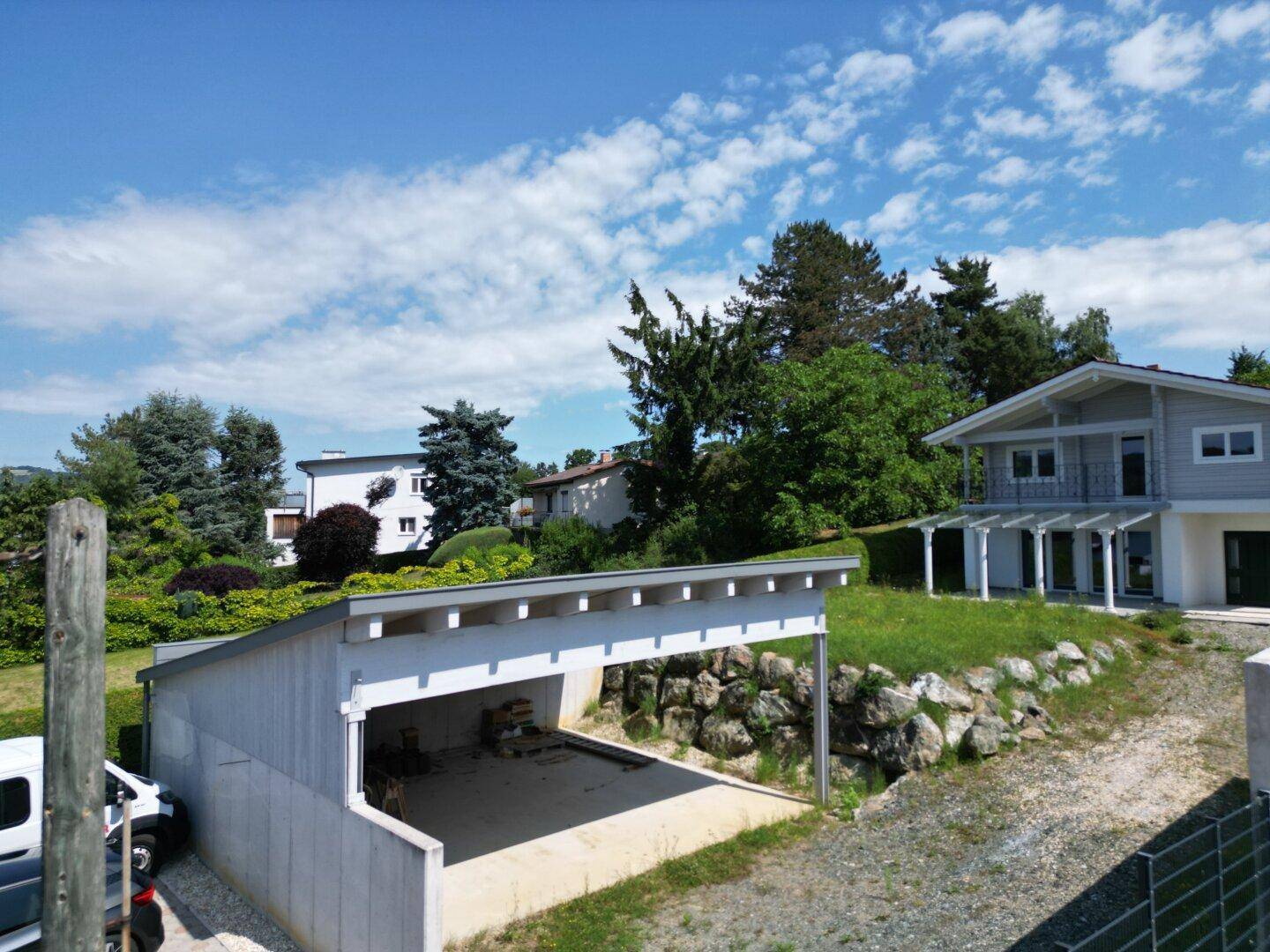 Ansicht des Hauses mit Carport und Zufahrt, eingebettet in eine grüne Hügellandschaft.