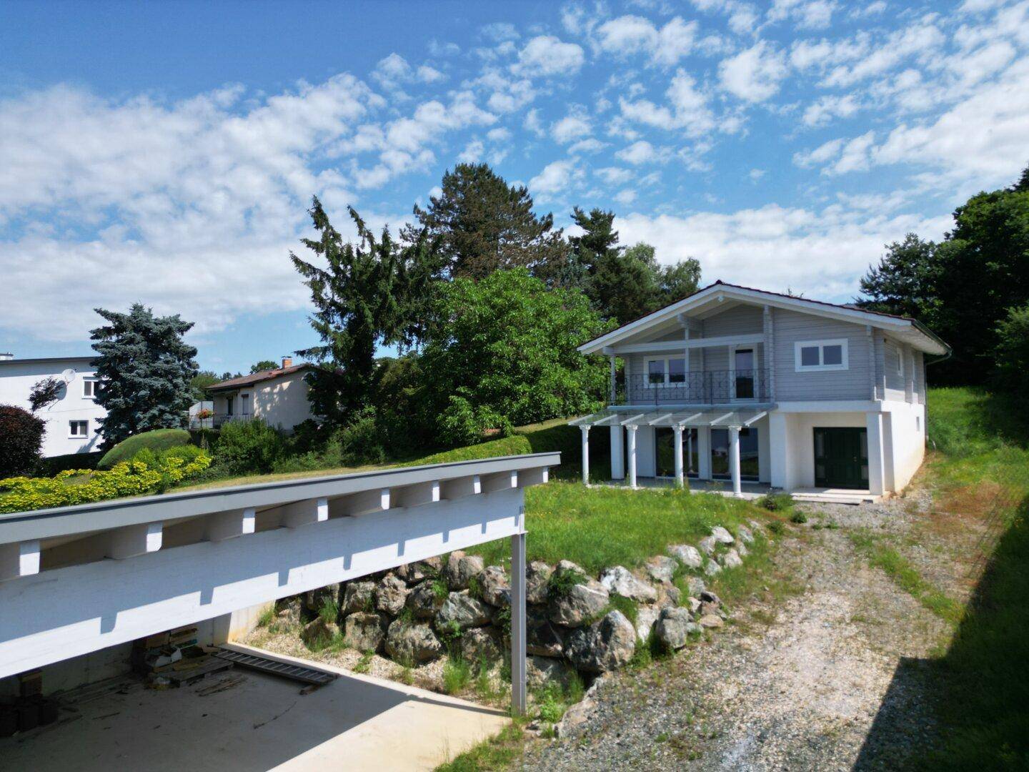 Außenansicht des Hauses mit Carport und grüner Umgebung unter blauem Himmel.