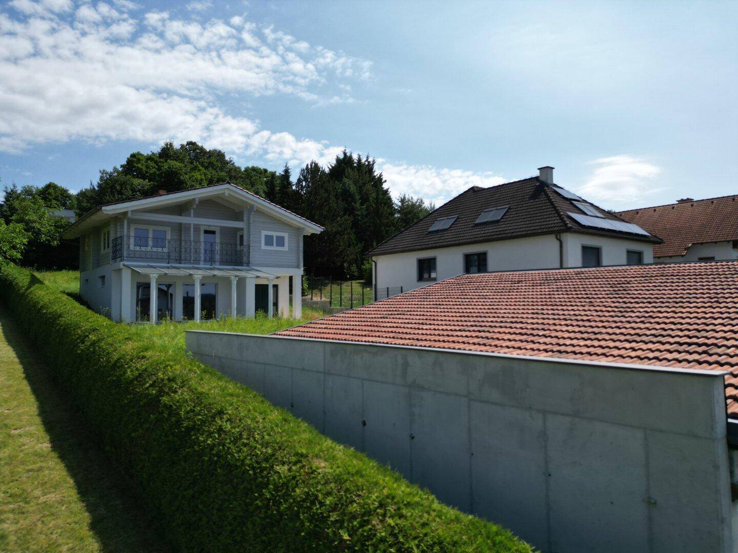Haus mit Satteldach und Photovoltaikanlage, umgeben von Hecken und Grünflächen.