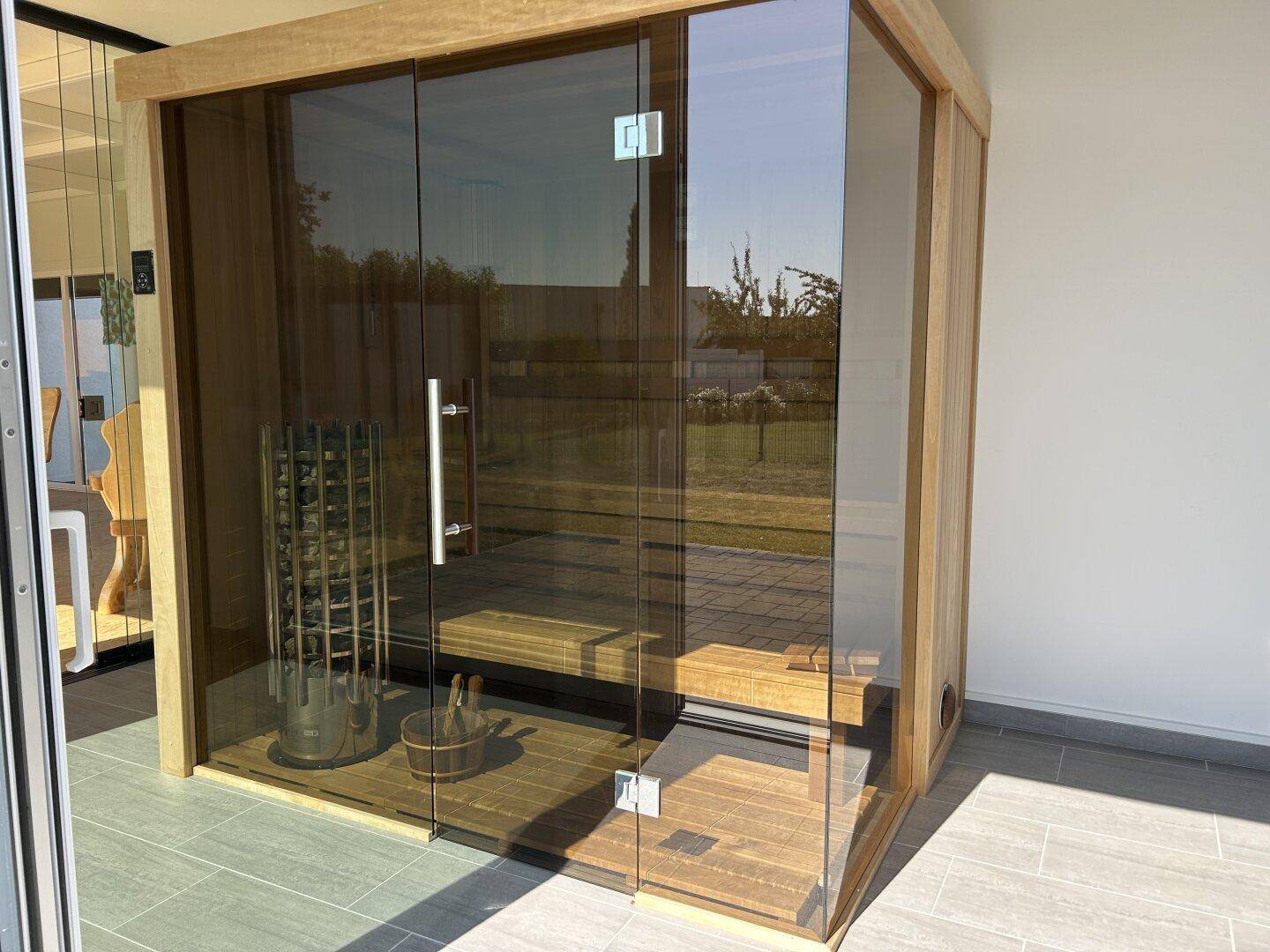 Moderne Glas-Saunakabine mit Holzinterieur und Heizofen, direkt am Wohnbereich gelegen.