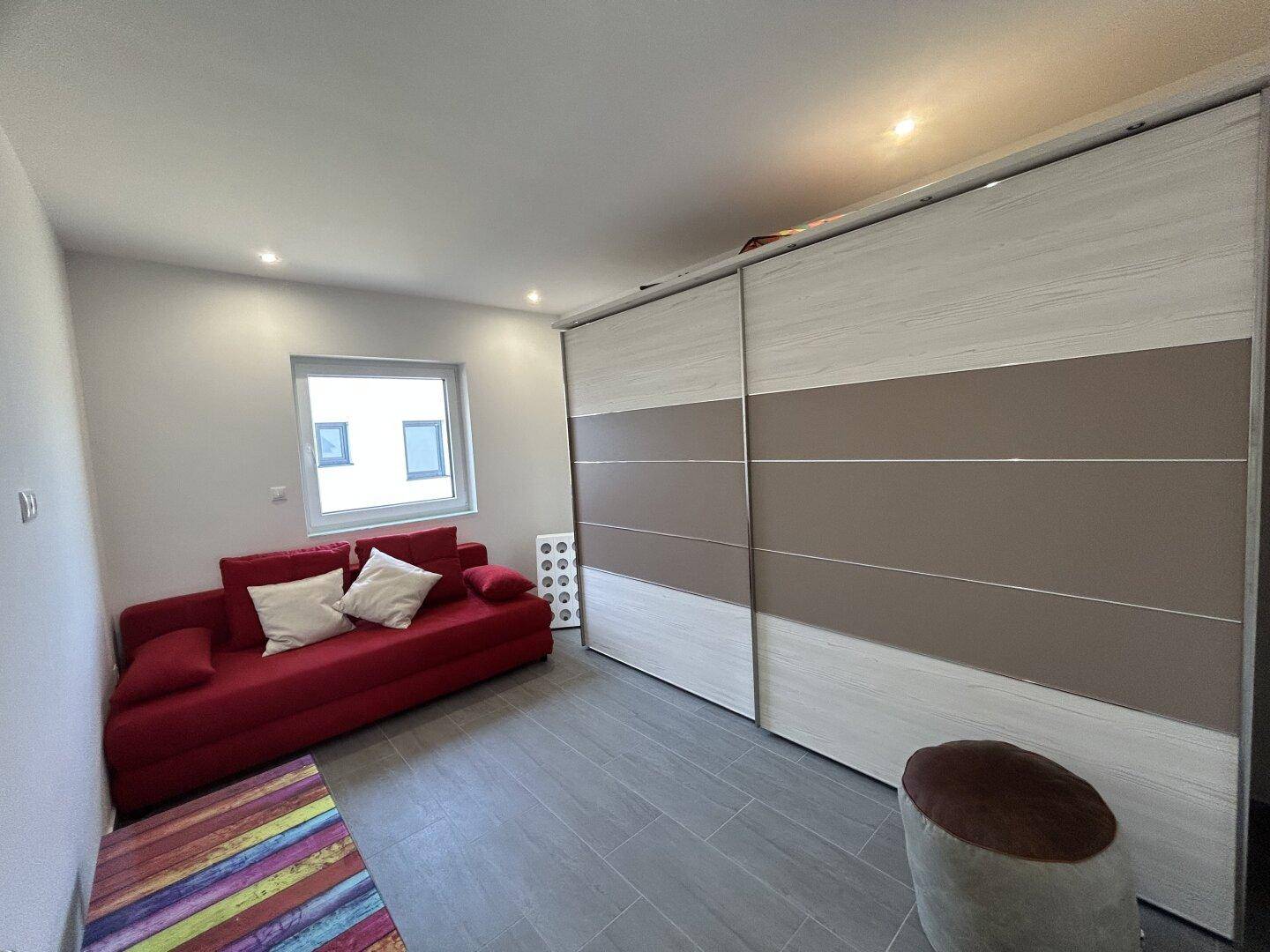 Gemütliches Schlafzimmer mit rotem Sofa, großem Schiebeschrank und hellem Fliesenboden.