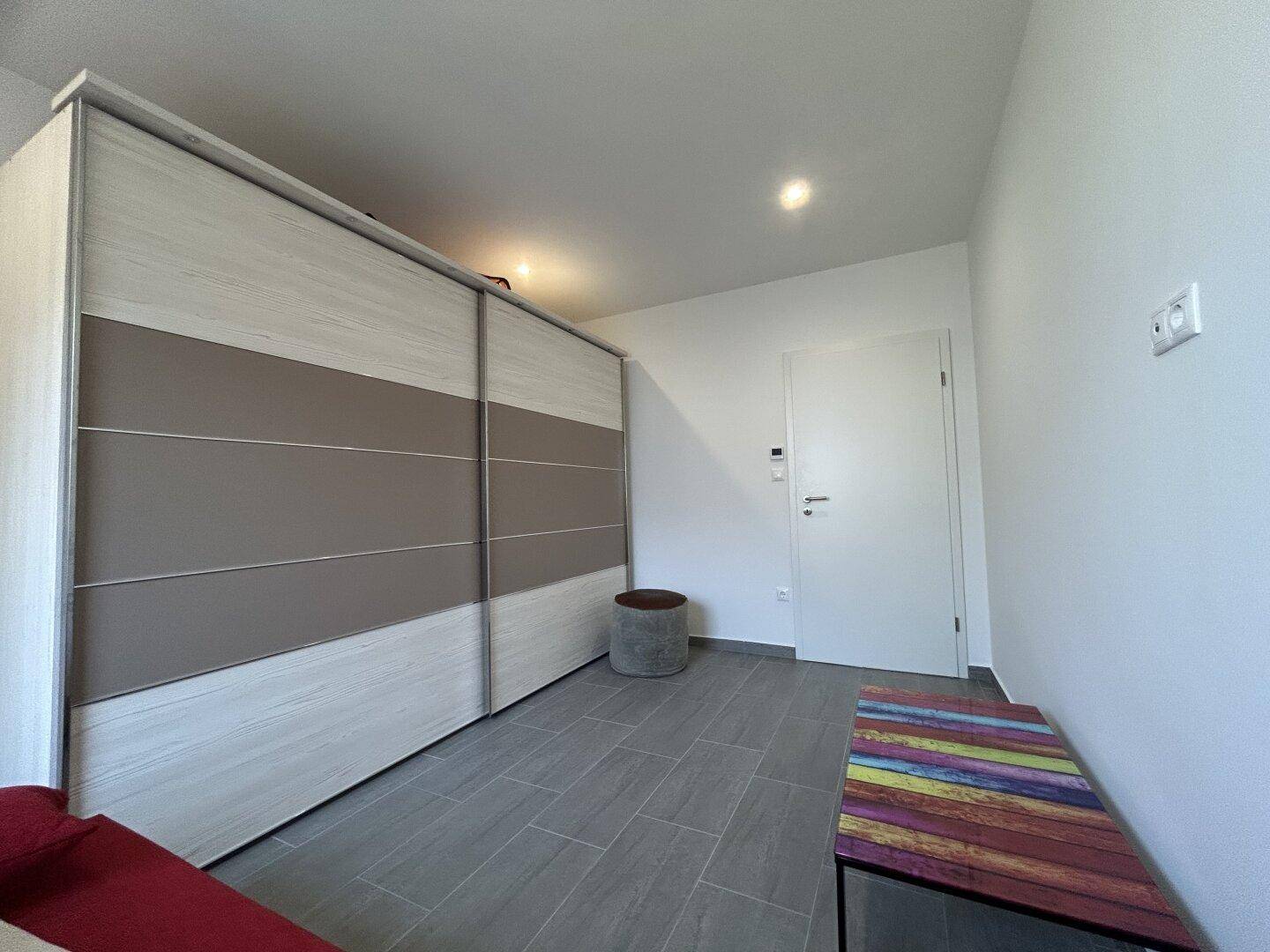 Schlafzimmer mit großem Schiebeschrank, hellem Fliesenboden und weiß gestrichenen Wänden.
