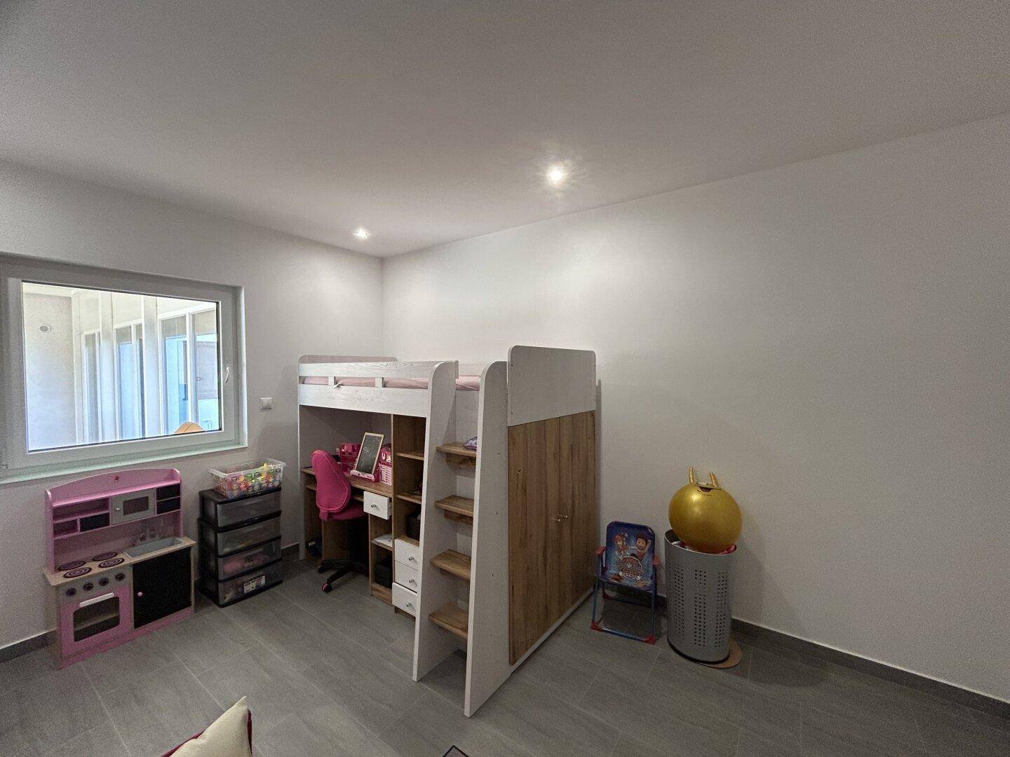Kinderzimmer mit Hochbett, Schreibtisch und Spielküche am Fenster, hell und freundlich.