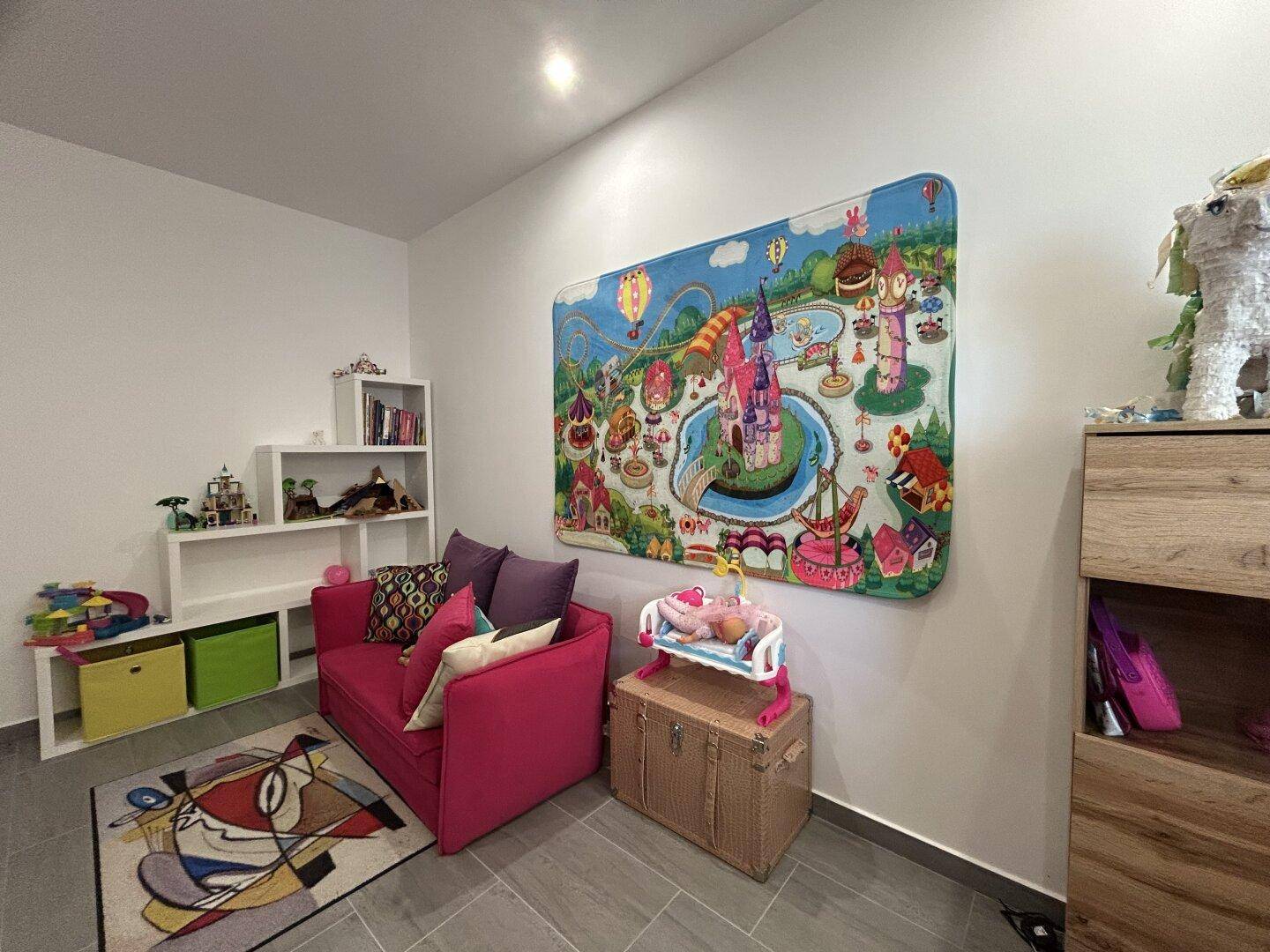 Farbenfrohes Kinderzimmer mit Spielteppich, rosa Sofa und weißen Regalen für Spielzeug.