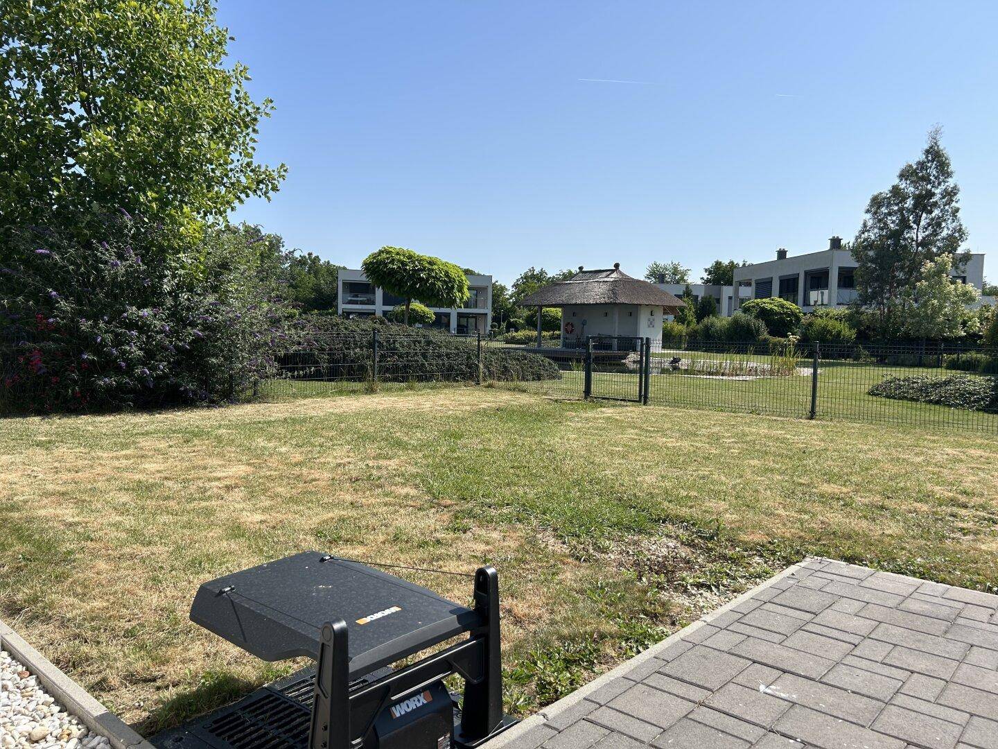 Gartenbereich mit Rasenfläche, Grill und Blick auf den Teich sowie die umliegenden Häuser.