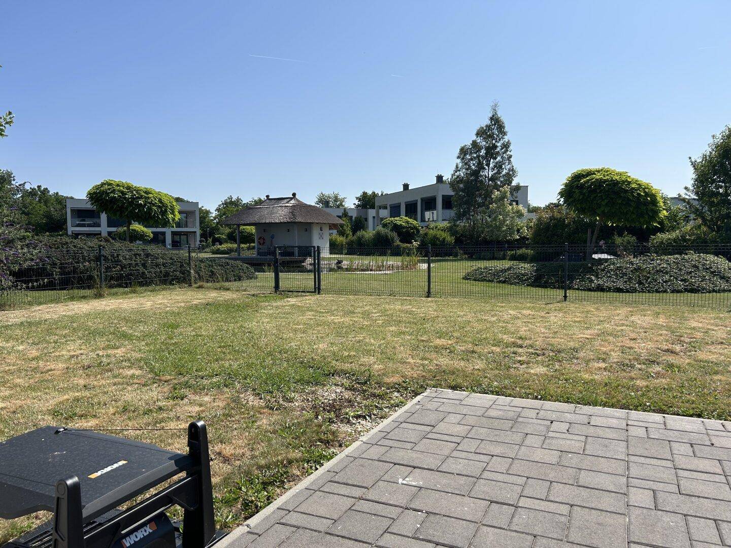 Gepflegter Garten mit Rasenfläche, Grill und Blick auf die Teichanlage und die Nachbarhäuser.