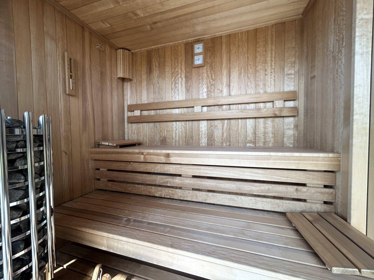 Innenansicht einer holzvertäfelten Sauna mit Bänken und traditionellem Saunaofen.