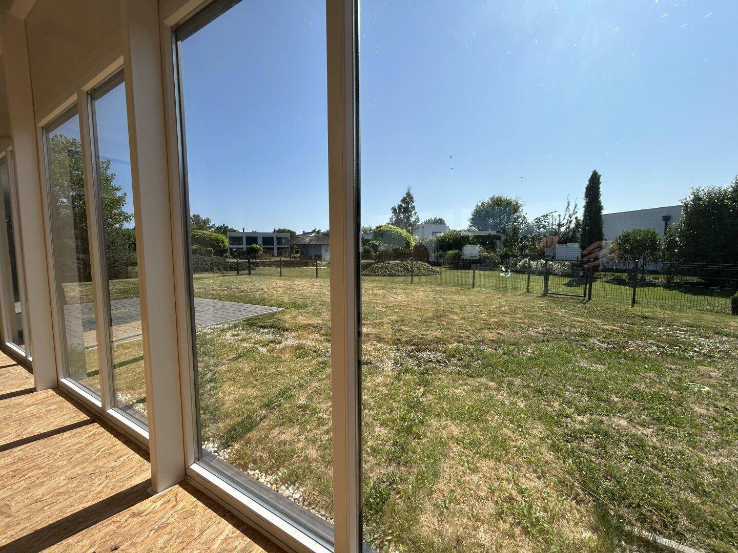 Blick aus dem Wintergarten in den weitläufigen Gartenbereich mit viel Grün und klarem Himmel.