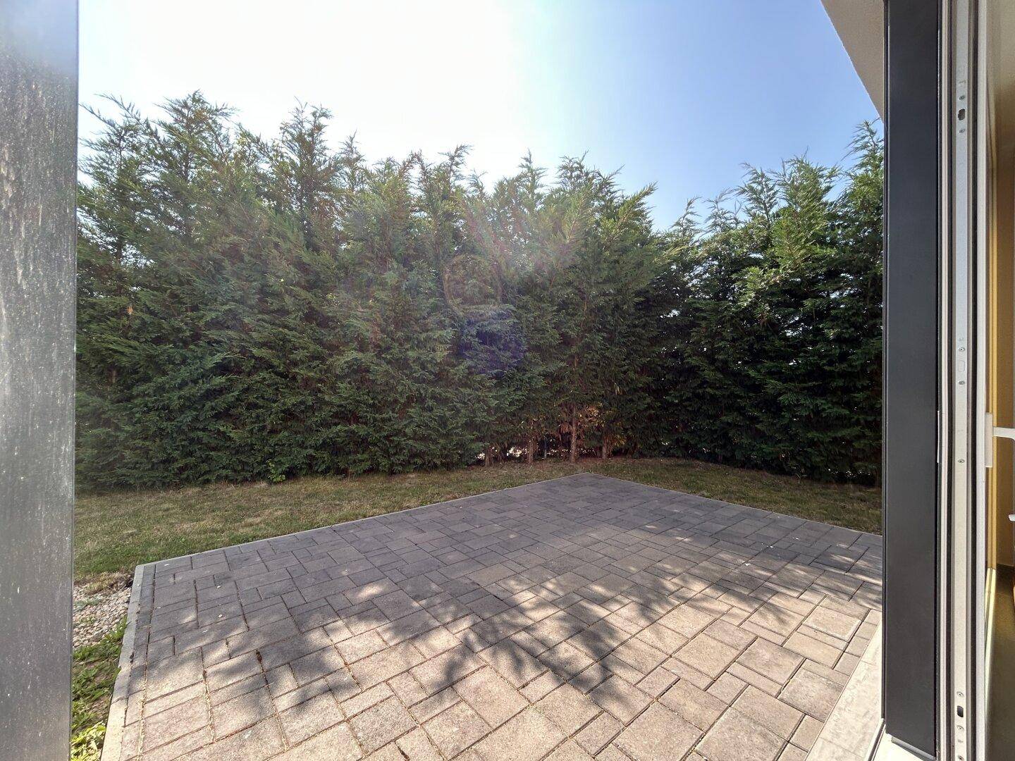 Blick auf die gepflasterte Terrasse, umgeben von einer dichten Hecke, die Privatsphäre bietet.