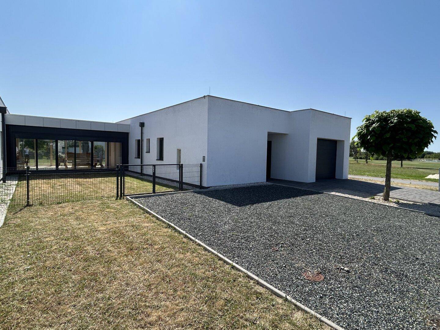 Vorderansicht eines modernen Hauses mit weißer Fassade, Kiesauffahrt und einem kleinen Vorgarten.