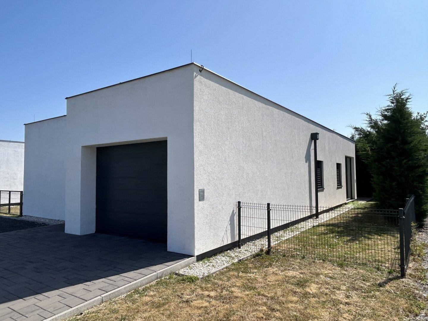 Seitenansicht eines modernen Hauses mit weißer Fassade und einem dunklen Garagentor.