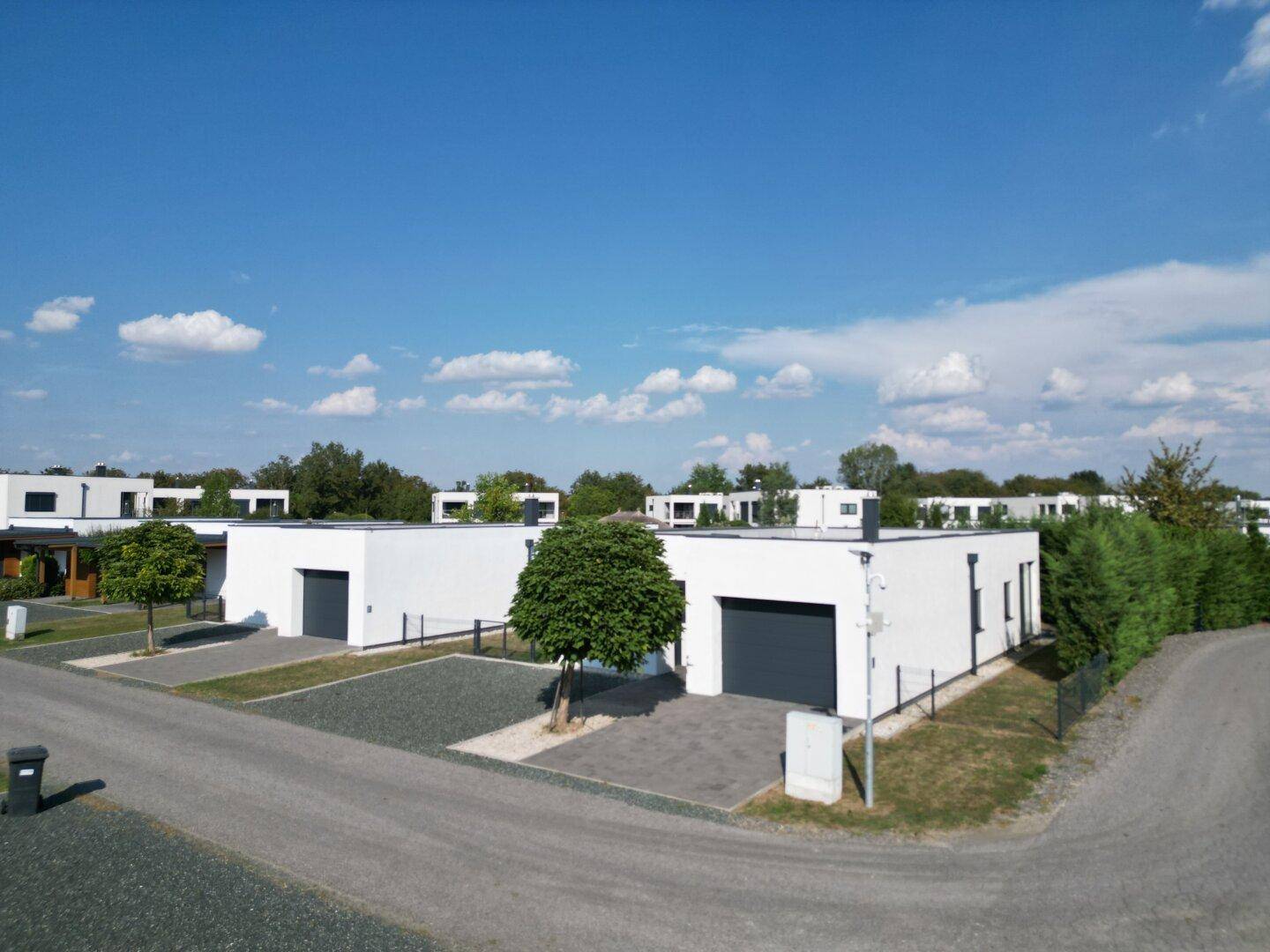 Moderne Einfamilienhäuser mit Flachdächern und Garagen in einer Wohnsiedlung unter blauem Himmel.