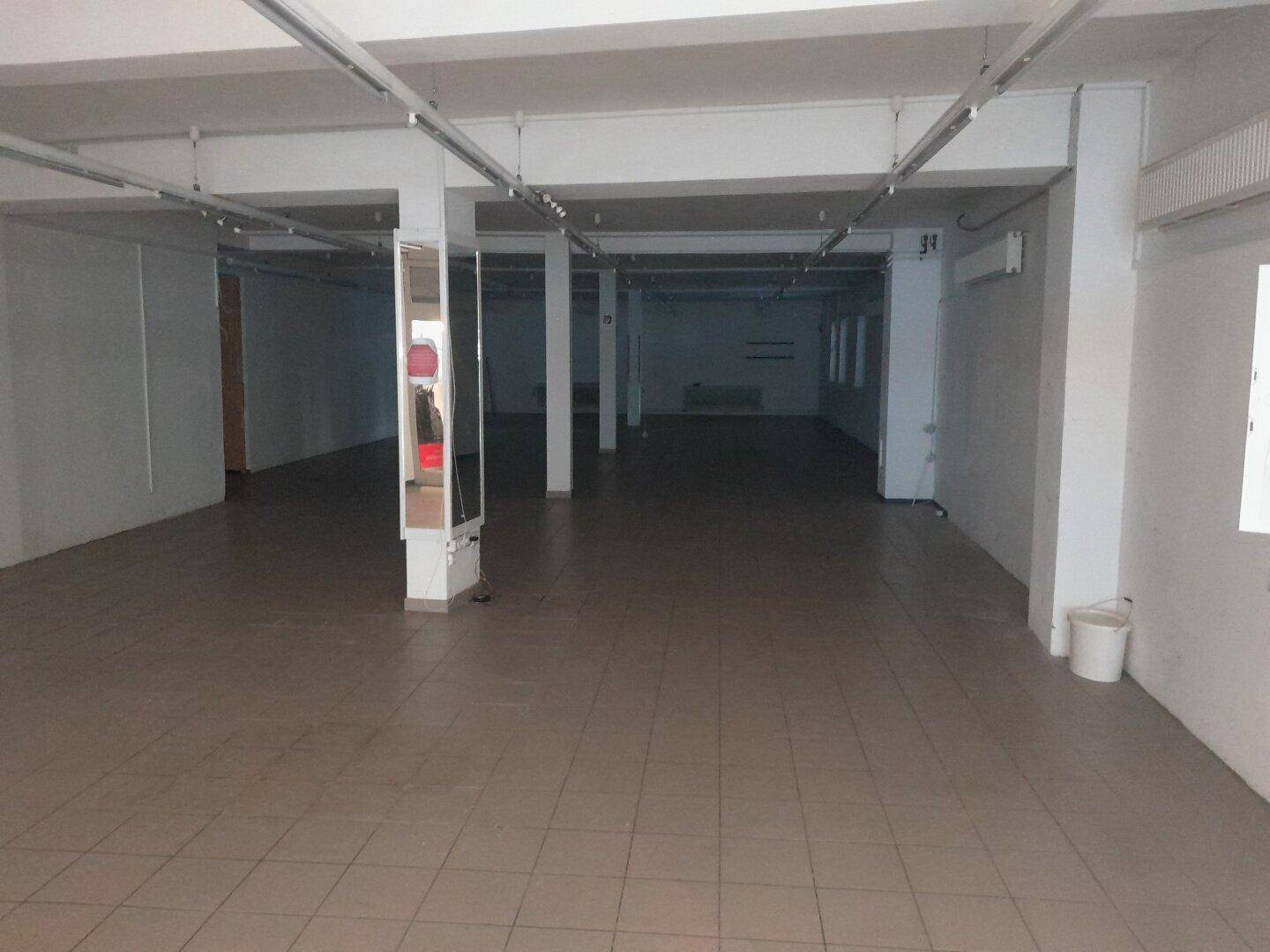 Großer, leerer Ladenraum mit Fliesenboden, Säulen und Deckenbeleuchtung, ideal für gewerbliche Nutzung.