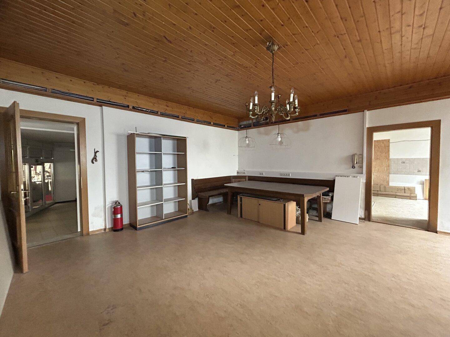 Rustikaler Raum mit Holzbalkendecke, Holztisch und Sitzbank, bereit für eine Renovierung.