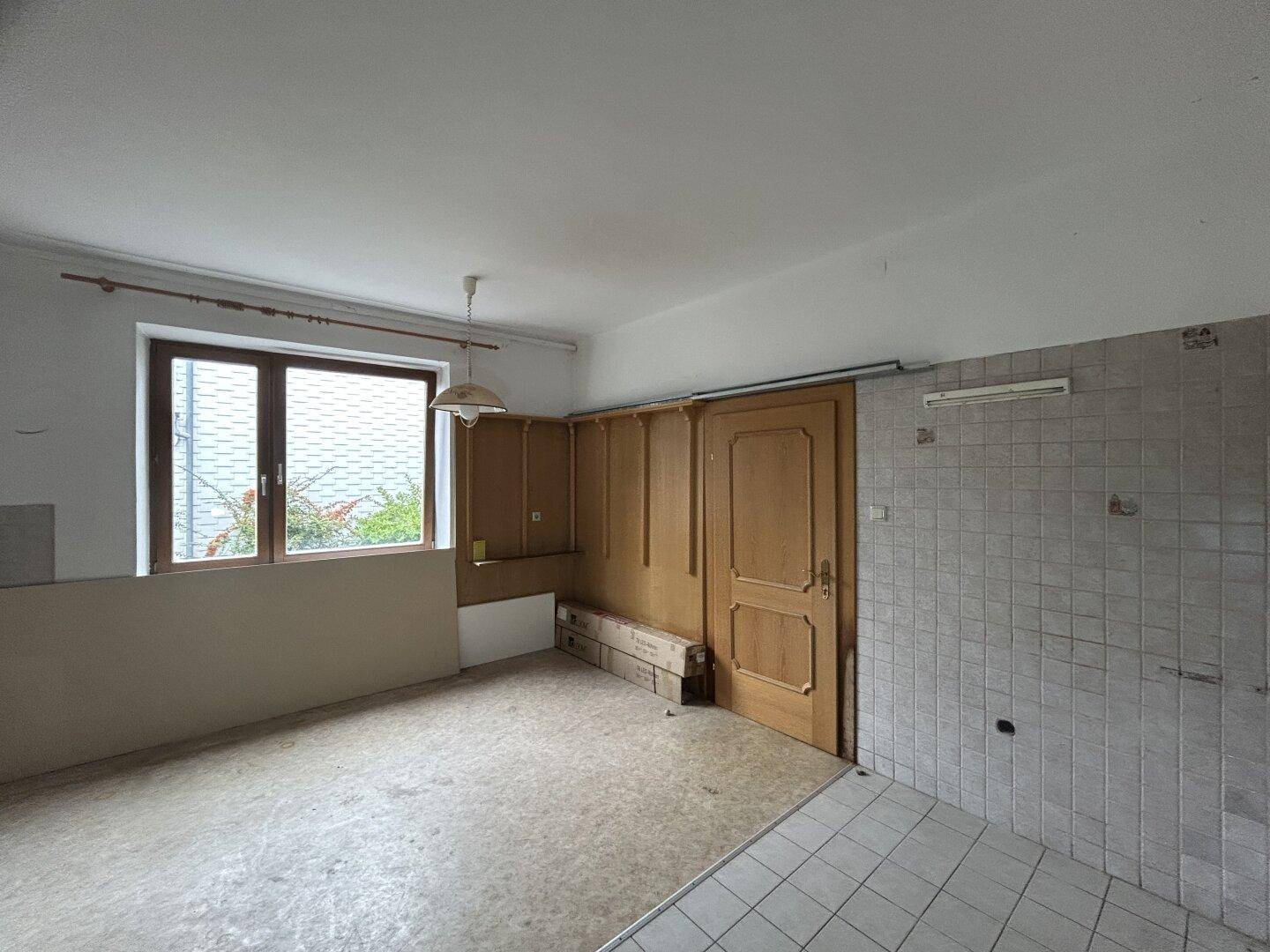 Küche mit Fenster, teilweise gefliesten Wänden und älteren Holzverkleidungen, die eine Modernisierung benötigt.