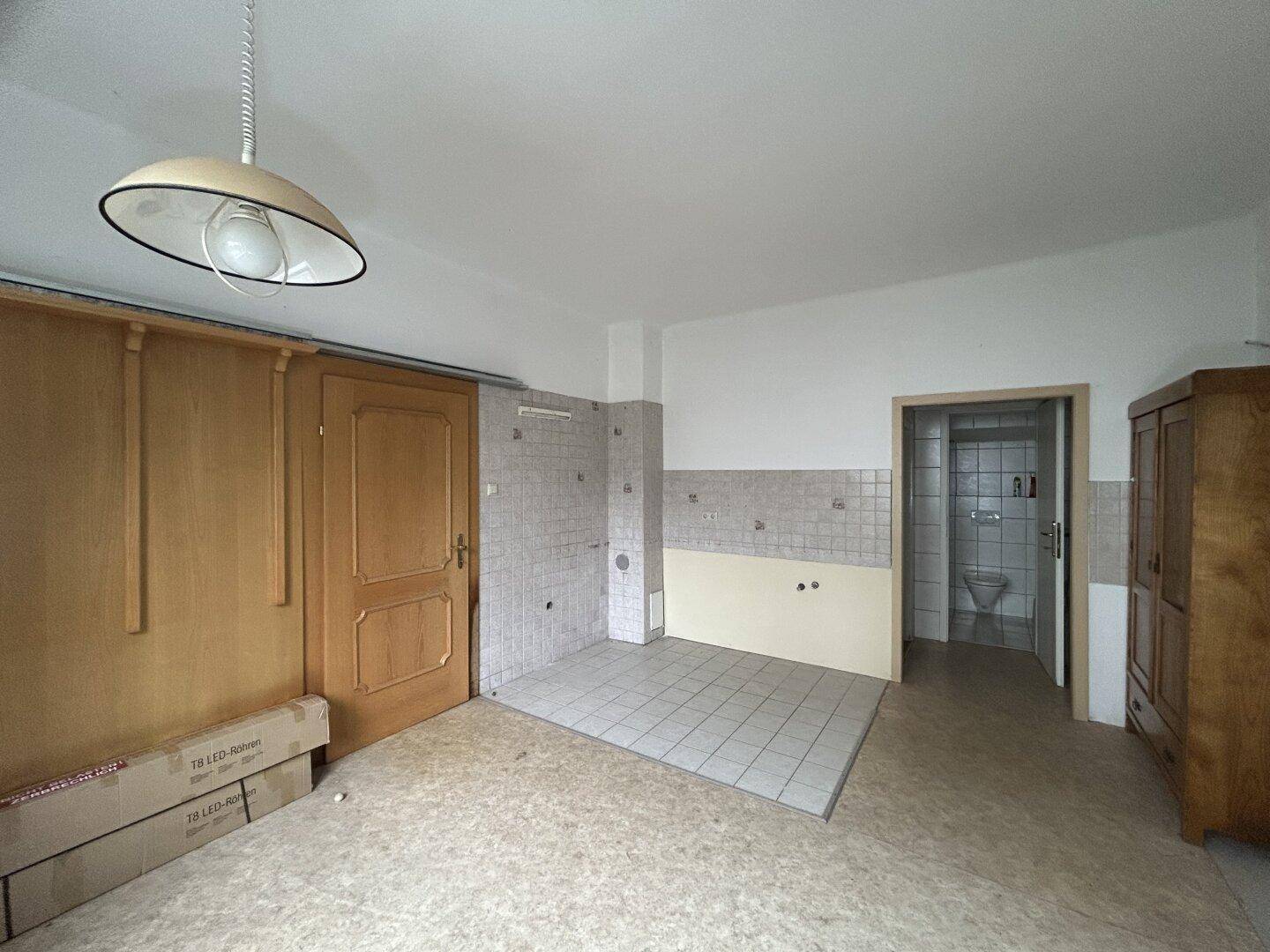 Ältere Küche mit Fliesenboden und teilweise gefliesten Wänden, die auf eine Renovierung wartet.