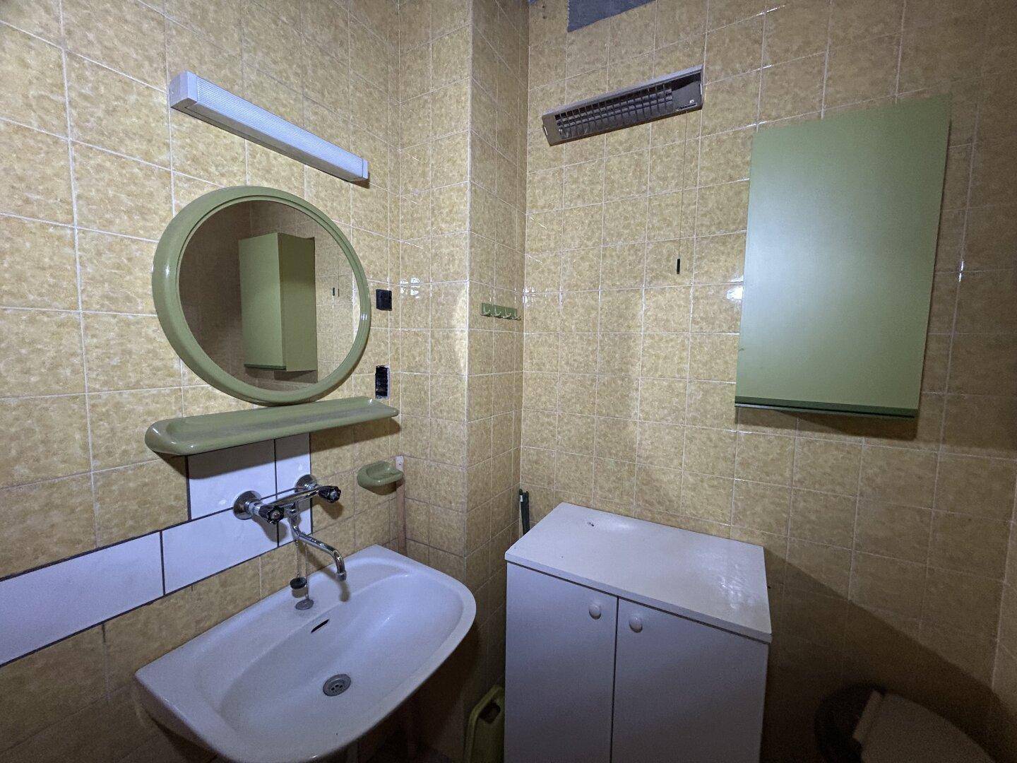 Badezimmer mit gelben Fliesen, Waschbecken und Spiegel, das eine Modernisierung benötigt.