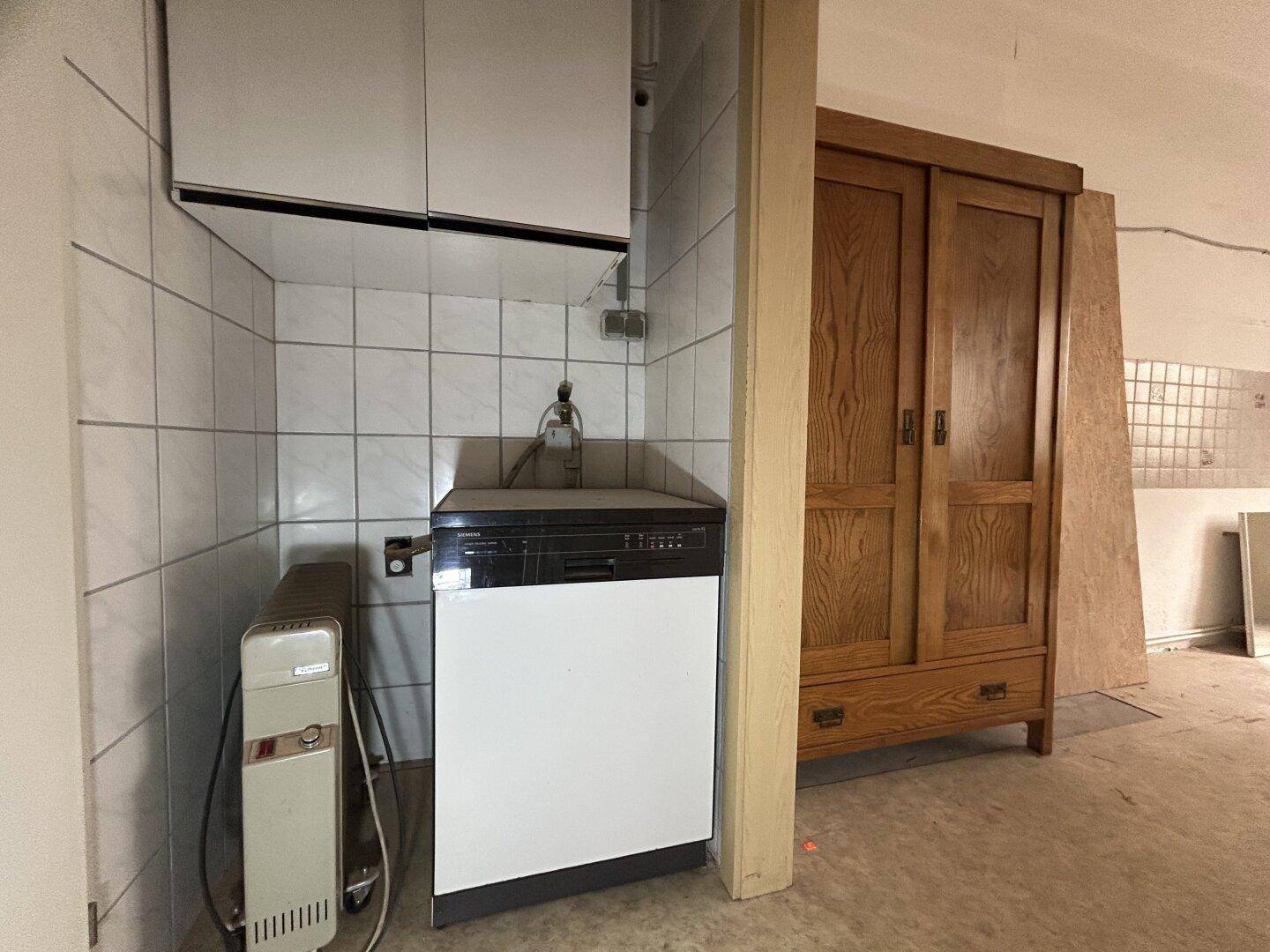 Küchenbereich mit Spülmaschine, Oberschränken und einem Holzschrank, der renoviert werden muss.