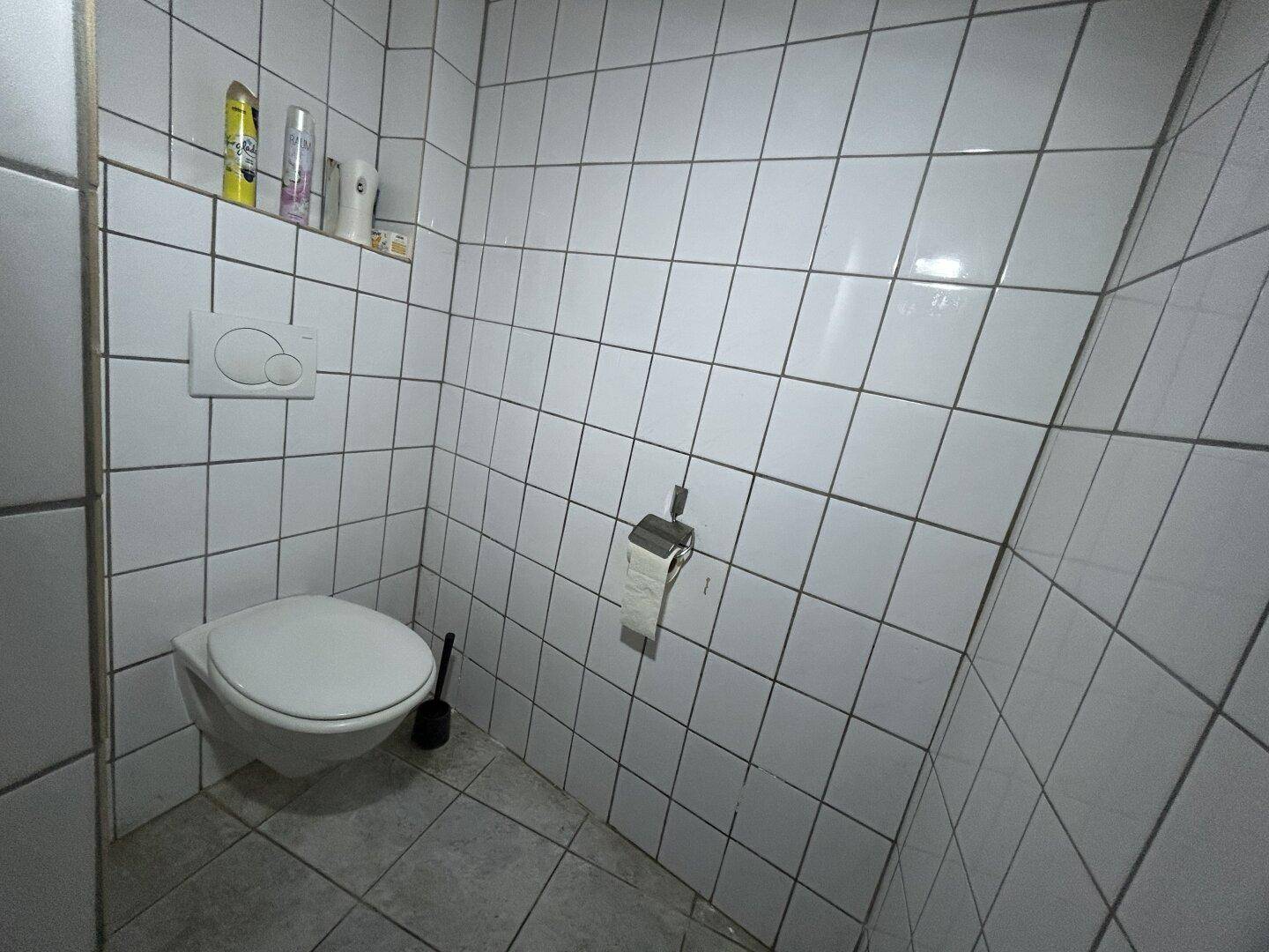 Separate Toilette mit weißen Fliesen und wandhängendem WC, in einem einfachen, funktionalen Zustand.