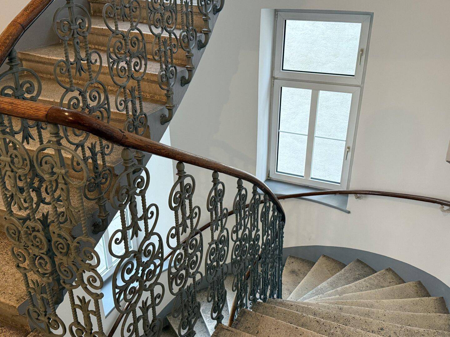 Historisches Treppenhaus mit schmiedeeisernem Geländer und Steinstufen.