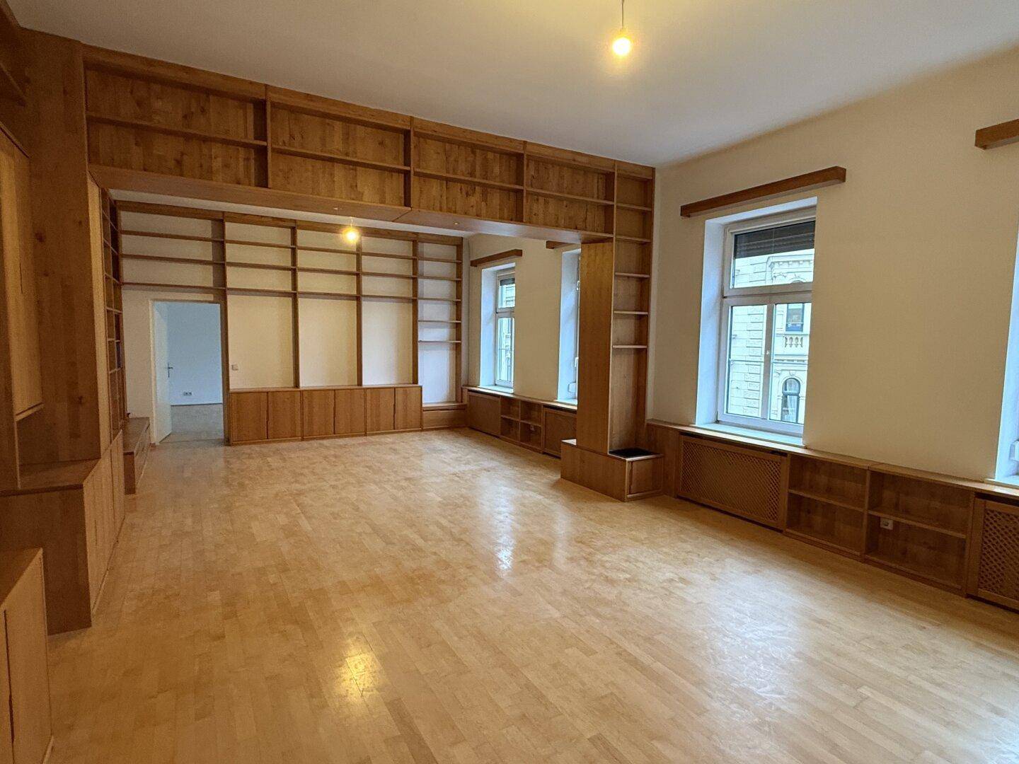Großes Wohnzimmer mit maßgefertigten Holzregalen, Parkettboden und hohen Decken.
