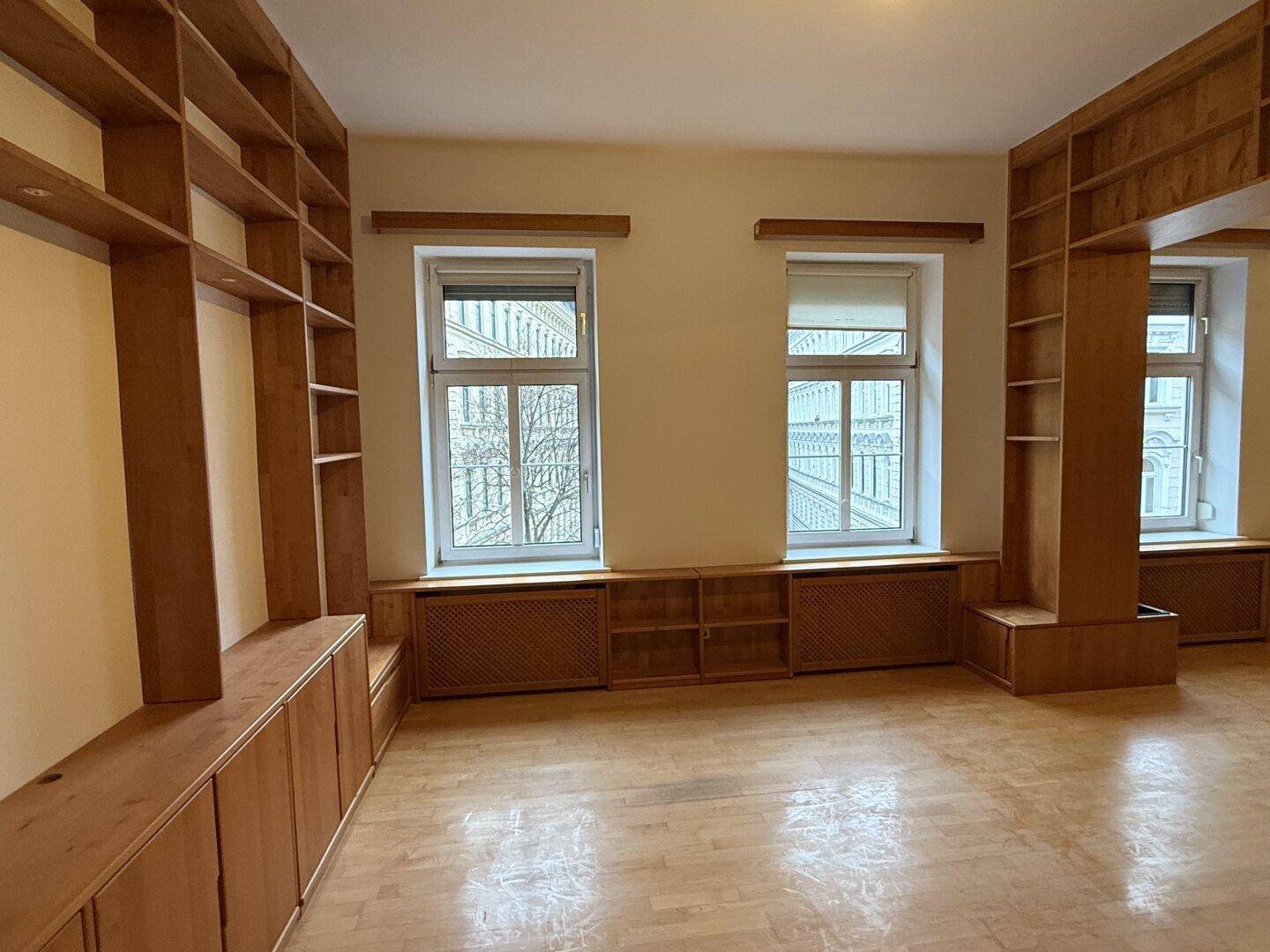 Heller Wohnraum mit maßgefertigten Holzregalen, Parkettboden und großen Fenstern.