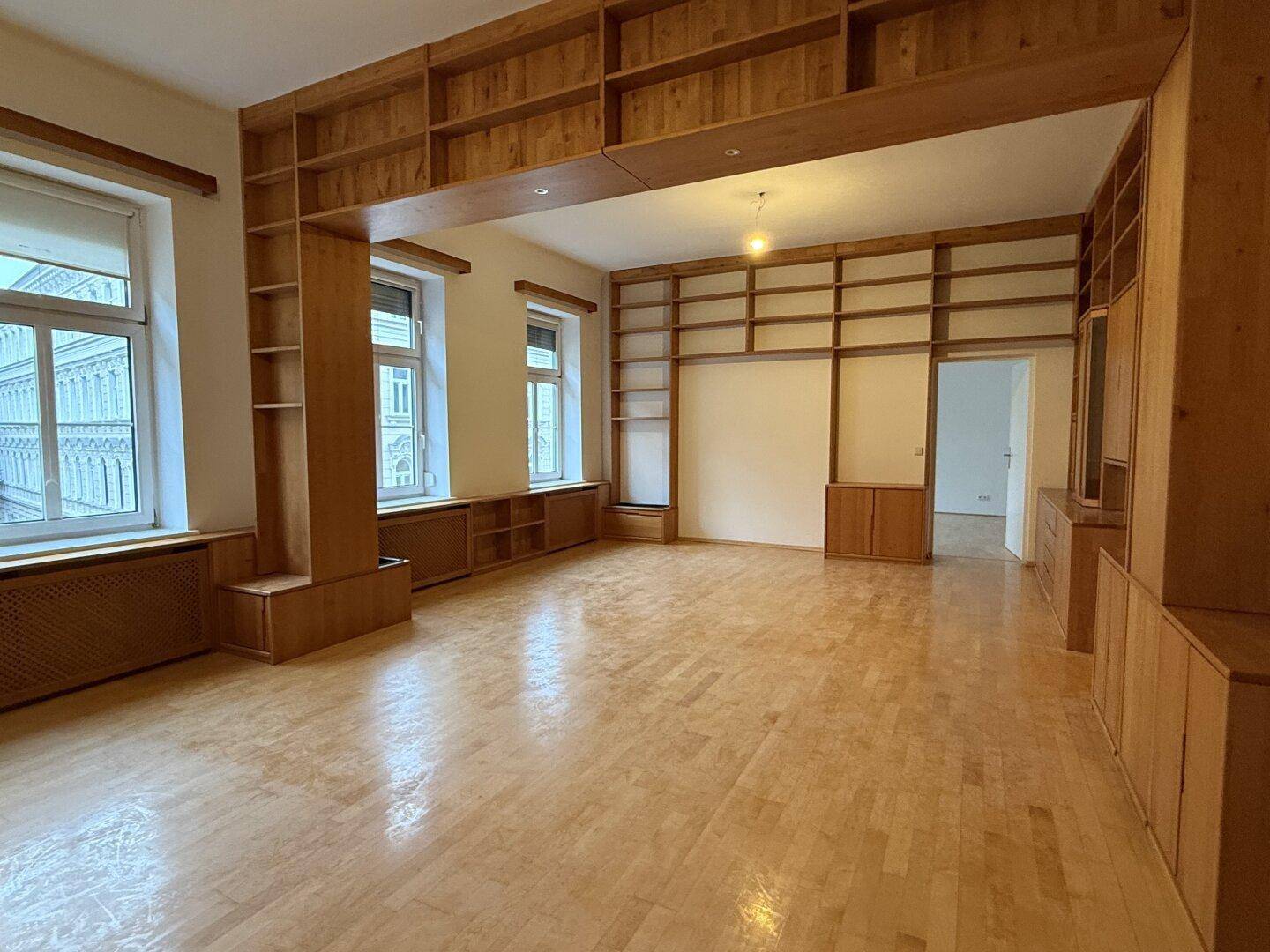Geräumiger Wohnbereich mit umfangreichen Holzregalen, Parkettboden und hohen Decken.