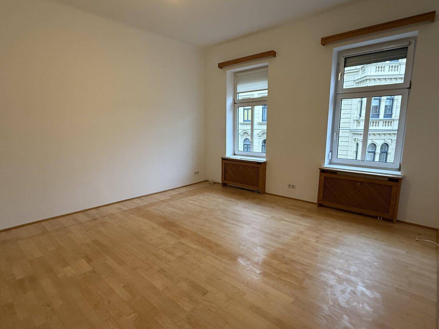 Leerer Raum mit Parkettboden, hohen Decken und großen Fenstern.