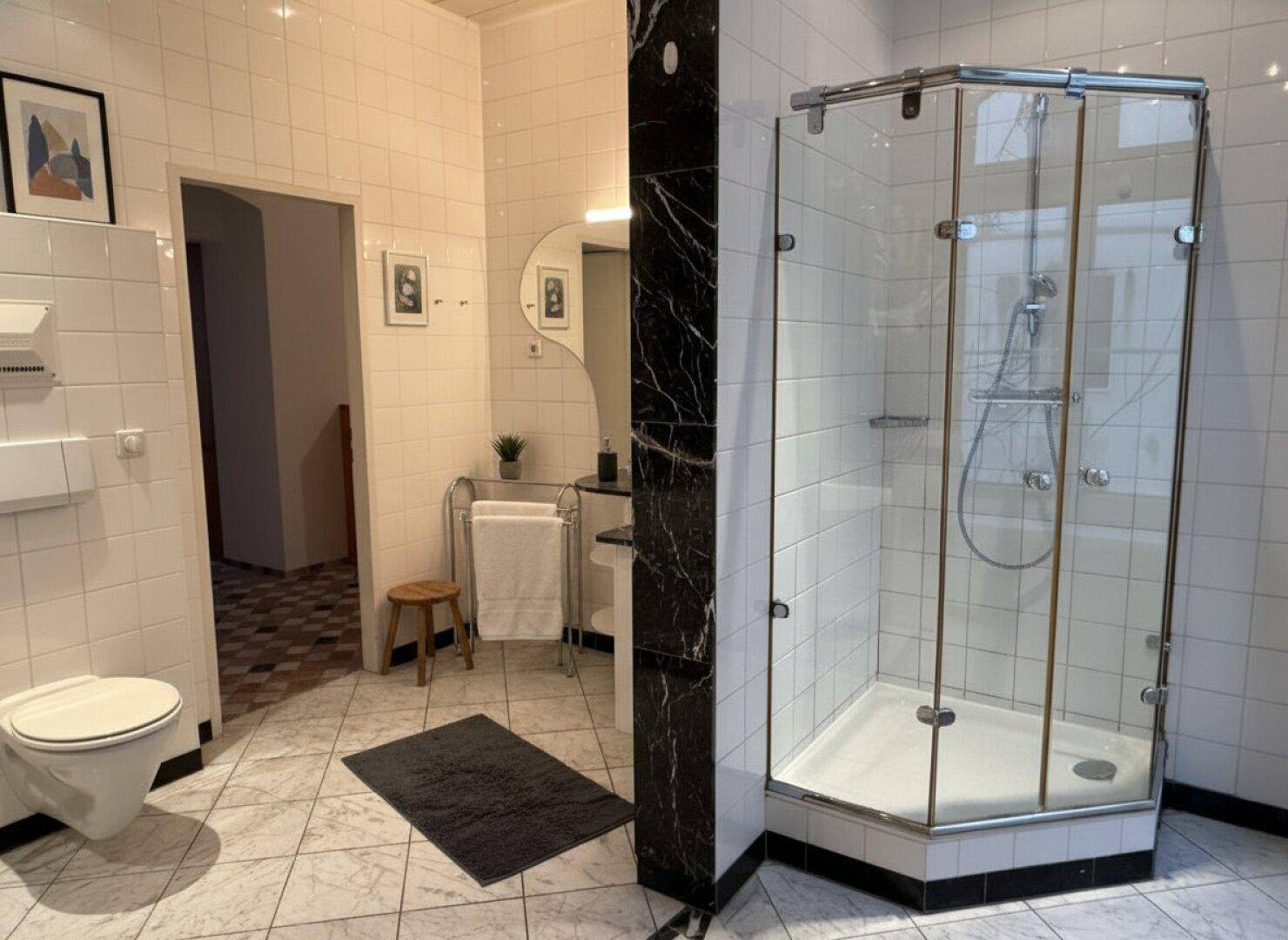 Badezimmer mit weiß gefliesten Wänden, schwarzem Marmor und einer modernen Duschkabine.