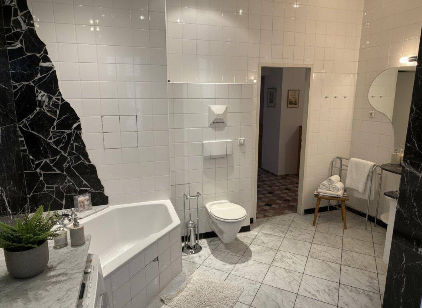 Geräumiges Badezimmer mit Eckbadewanne, wandmontierter Toilette und Marmorboden.