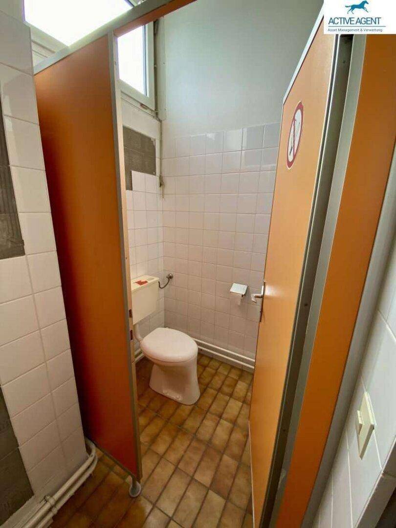 Toilettenkabine mit WC, gefliesten Wänden und orangefarbenen Trennwänden.