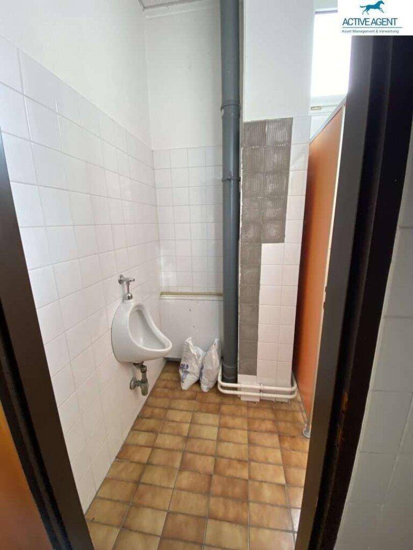 Waschraum mit Urinal, gefliesten Wänden und einem Fenster.