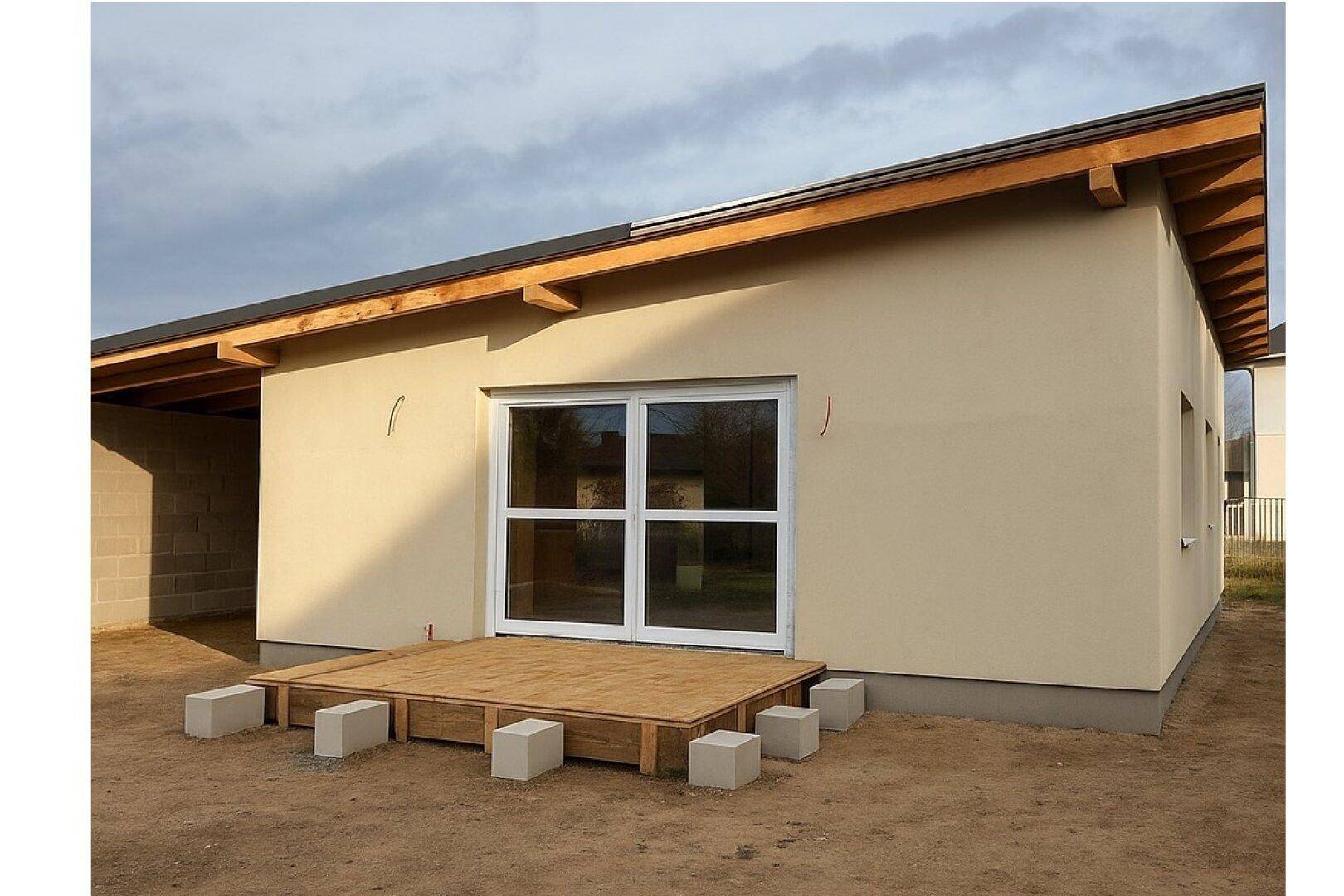 Seitenansicht des Neubaus mit großer Schiebetür und einer im Bau befindlichen Holzterrasse.