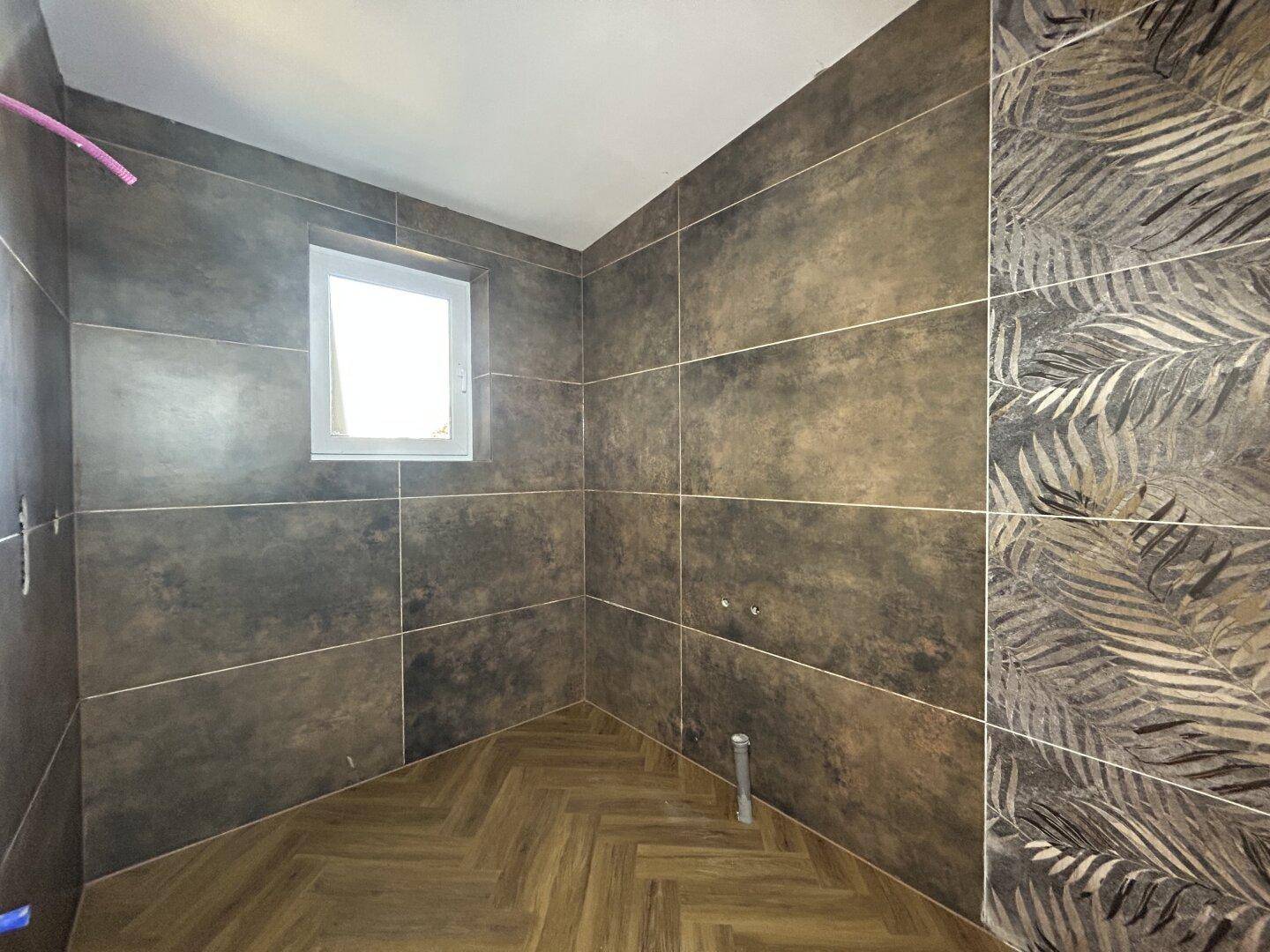 Badezimmer im Bau mit modernen großformatigen Fliesen und einem Fenster für natürliche Belüftung und Tageslicht.