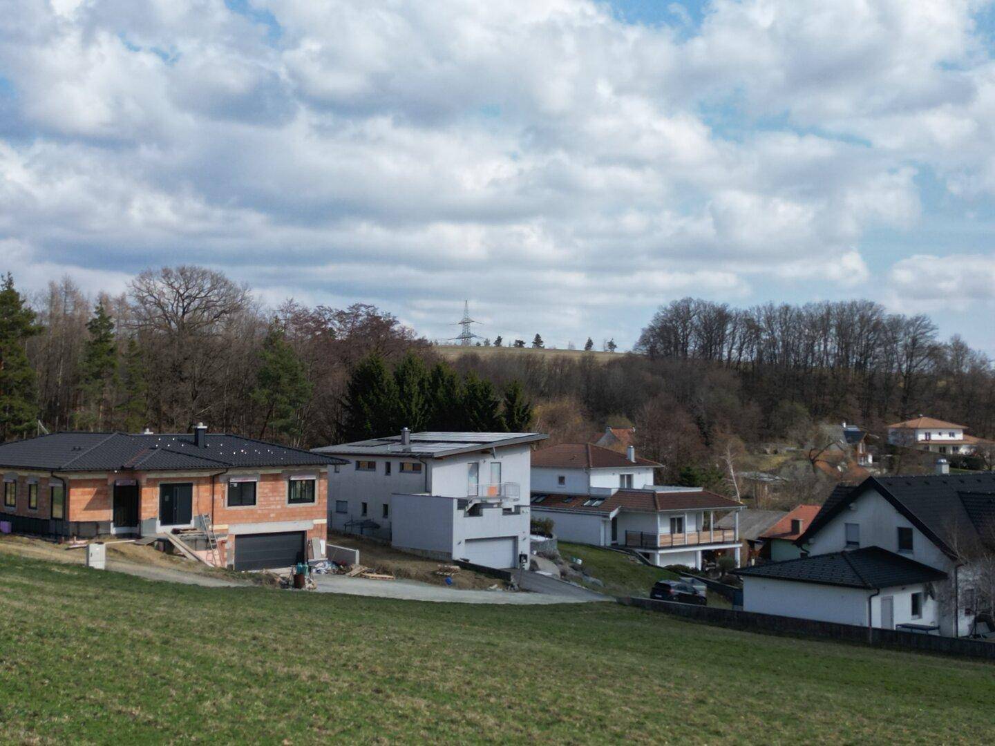 Blick auf eine Wohnsiedlung mit Neubauten und grüner Hügellandschaft im Hintergrund unter bewölktem Himmel.