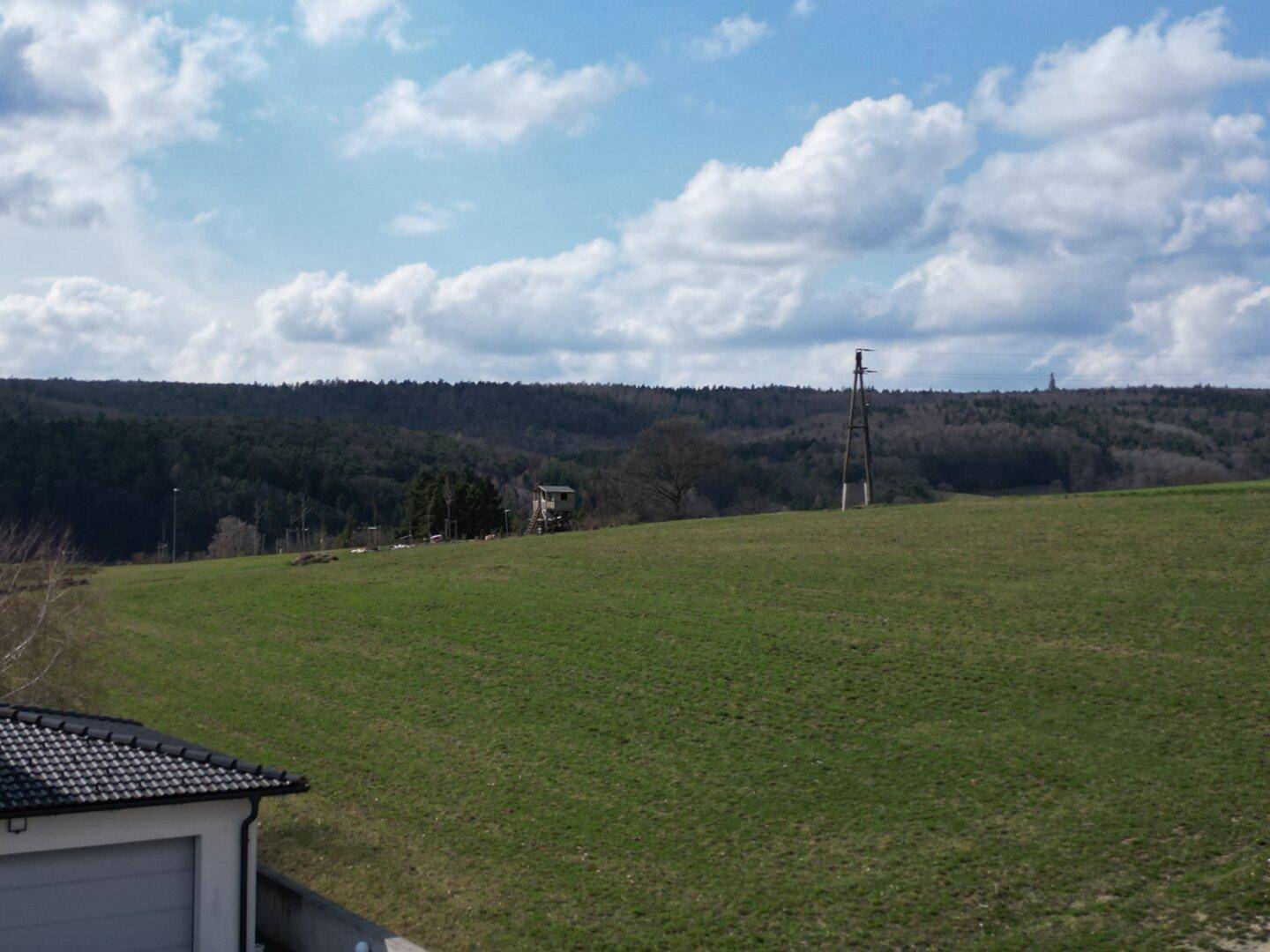 Panoramablick über grüne Wiesen und Wälder unter einem weiten Himmel mit vereinzelten Wolken.