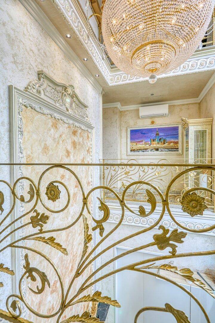 Luxuriöser Treppenaufgang mit goldener Balustrade, Kronleuchter und kunstvollen Wandverzierungen, sehr elegant.