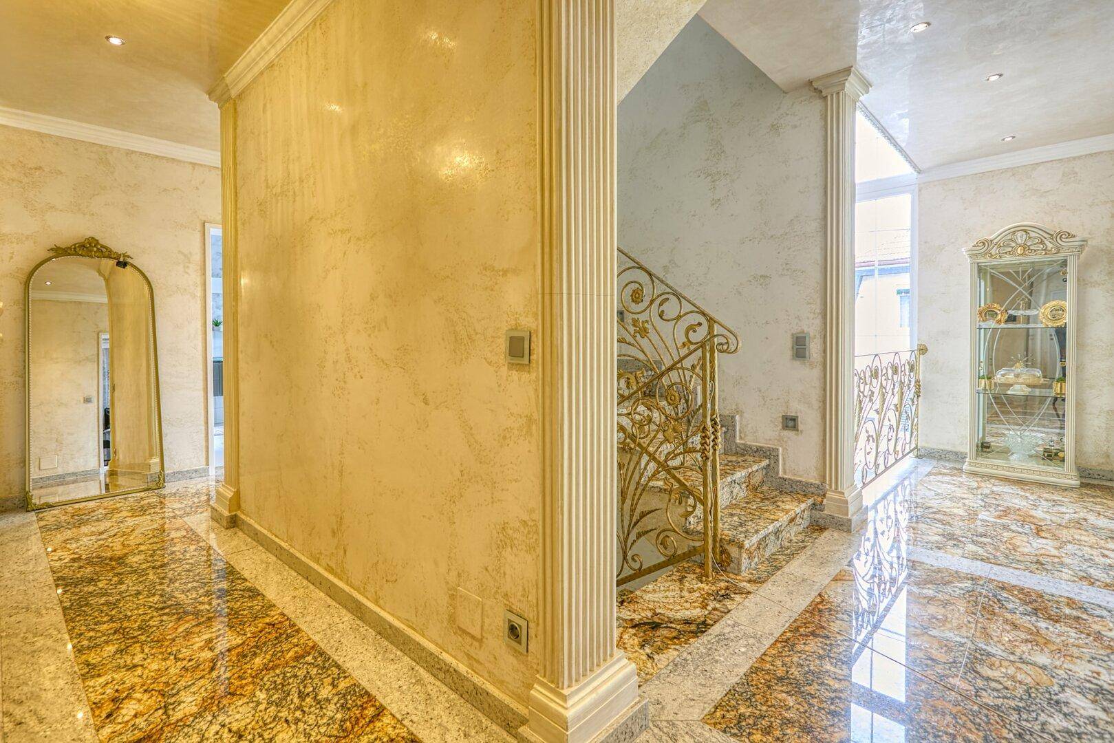 Prunkvoller Flur mit Marmorboden, geschwungener Treppe und dekorativen Säulen, sehr hell.
