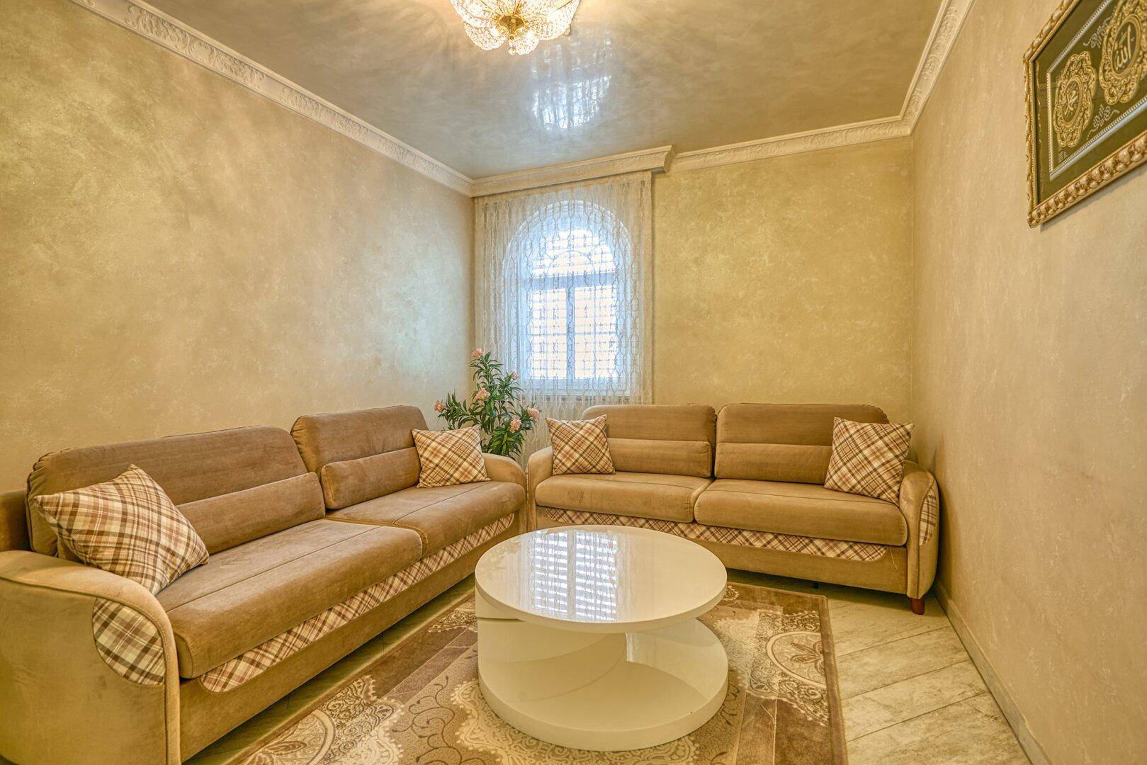 Gemütliches Wohnzimmer mit beigen Sofas, Couchtisch und einem Fenster mit Vorhängen, gut gepflegt.